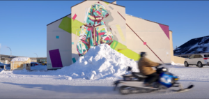 Person on snowmobile rides past mural of polar bear above mound of snow.